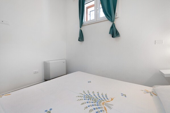 Une chambre à coucher avec un lit, un radiateur, une fenêtre avec des rideaux et une prise de courant au mur.