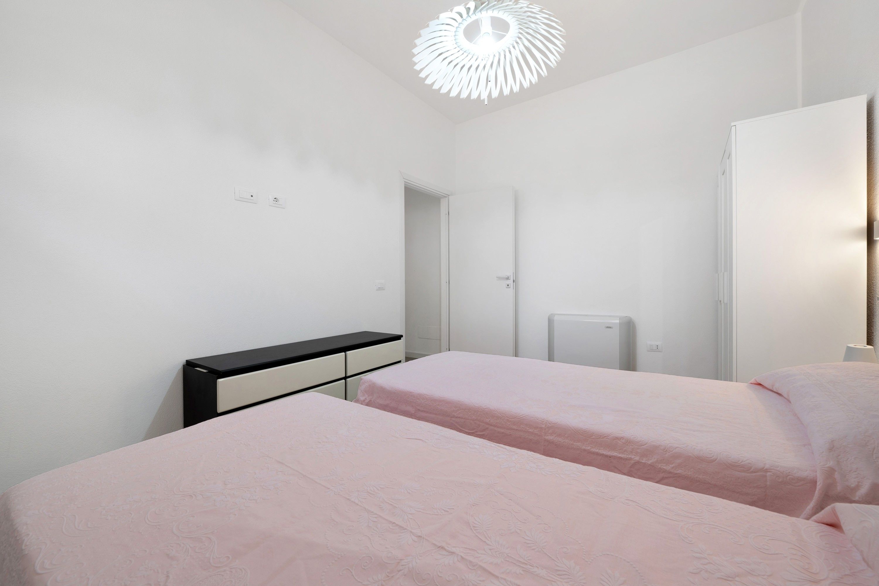 Una camera da letto con due letti, un armadio, un termosifone e una lampada a soffitto.