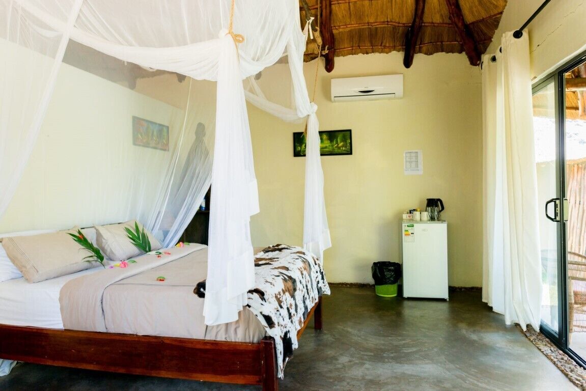 A room with a bed under a canopy, a small refrigerator, and a trash bin.
