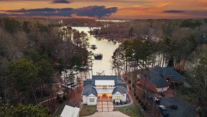 A large house with a driveway leading to a gated entrance, surrounded by trees and a body of water. - Waterfront Estate + Dock + Pool | Game Room | Sleeps 16 | Southern Belle Estate (Mooresville)