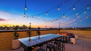 Un bar situé sur un toit, avec une table de baby-foot, des places assises en plein air, des guirlandes lumineuses et une vue sur la ville au coucher du soleil.