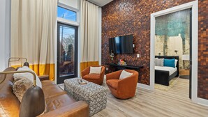 Un salon moderne comprenant un canapé, un fauteuil, un pouf et un téléviseur à écran plat fixé à un mur dont le motif rappelle celui d’un mur de briques.