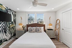 A bedroom with a large bed, two nightstands, a ceiling fan, a window with blinds, and a wall with a tropical leaf pattern. - Backyard + Golf Cart • Minutes to 30A + Beaches | The Little Blue Beach House (Santa Rosa Beach)