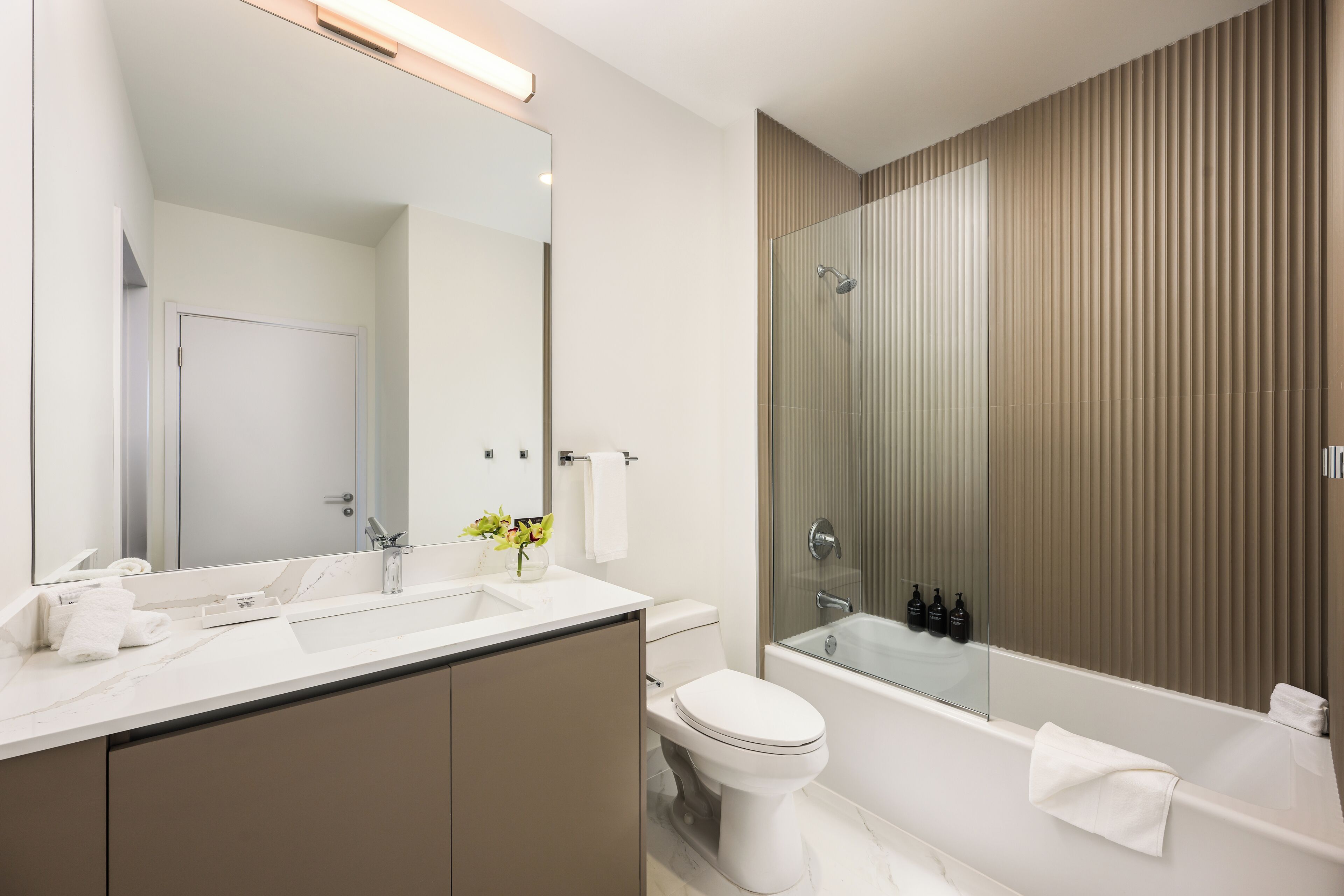 Een moderne badkamer met een grote spiegel, een toilet, een wastafel en een bad.