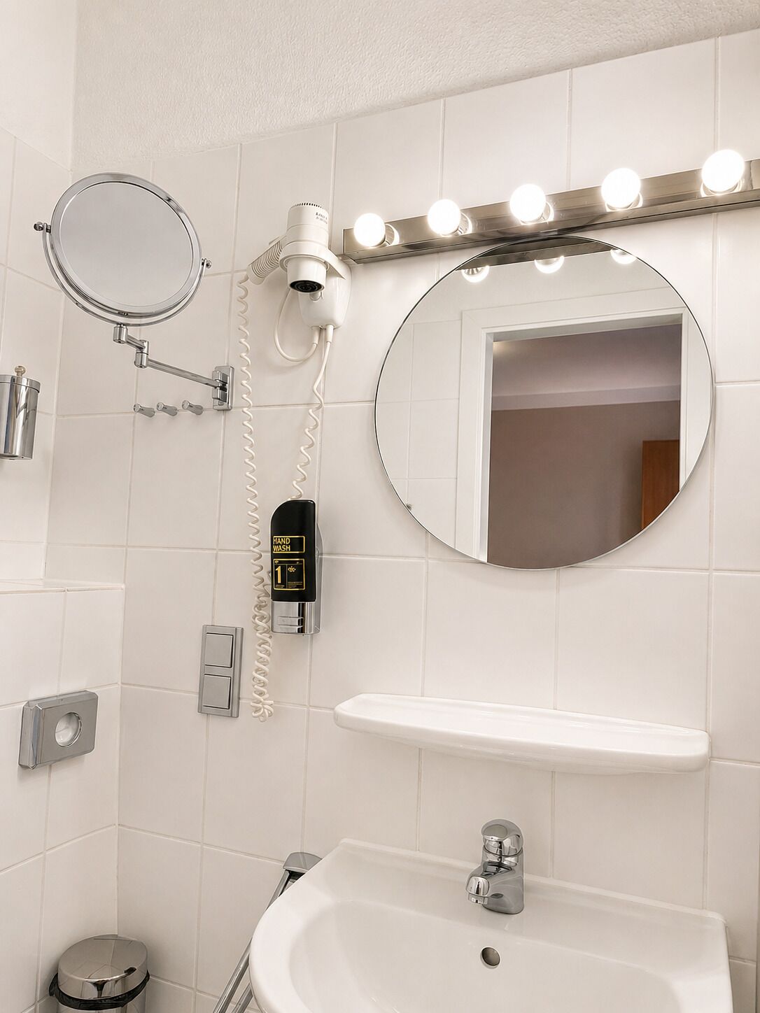 A bathroom with a sink, mirror, hand dryer, and vanity lights.