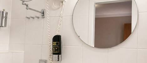 A bathroom with a sink, mirror, hand dryer, and vanity lights.