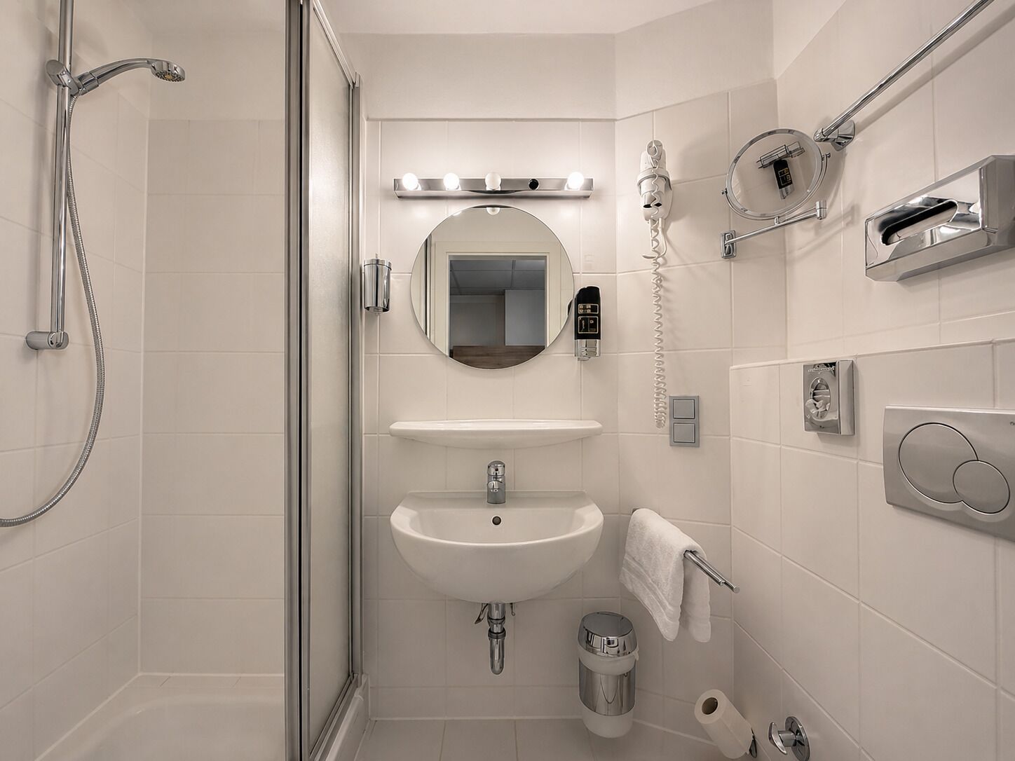 Un baño moderno con ducha, lavamanos, espejo y barra para toallas.