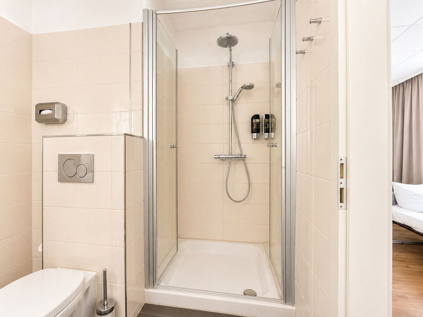 A glass-enclosed shower with a handheld showerhead and a wall-mounted faucet.
