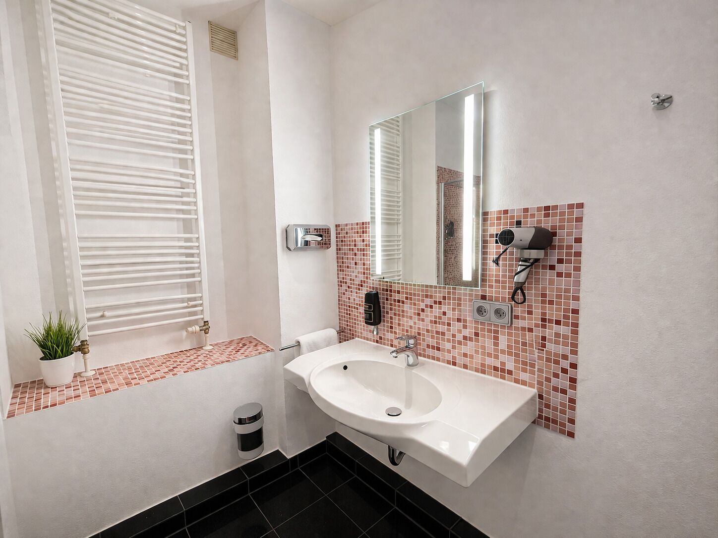 A bathroom with a white sink, a mirror, a towel rack, a hairdryer, and a small trash bin.