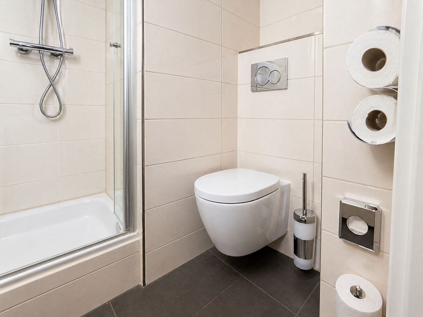 A modern bathroom with a shower, toilet, and toilet paper dispenser.