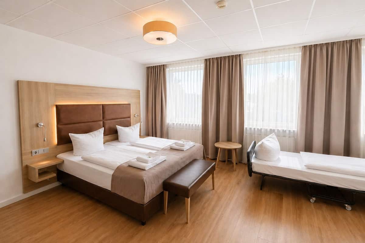 Camera d'albergo con un letto grande, un letto più piccolo, un comodino, una panca e un tavolino rotondo.