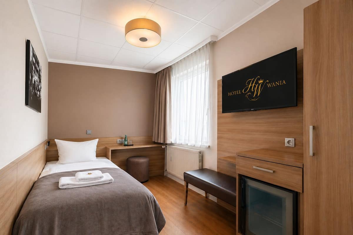 Camera d'albergo con un letto, comodino, panca, televisione e termosifone.
