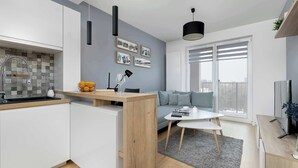 Eine moderne Küche mit weißen Schränken, einer Holzarbeitsplatte und einer gefliesten Spritzschutzleiste. Es gibt eine Essecke mit einem grauen Sofa und einem kleinen Tisch.