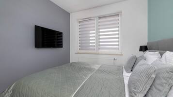Ein Schlafzimmer mit einem Bett, einem an der Wand befestigten Fernseher und einem Fenster mit Jalousien.