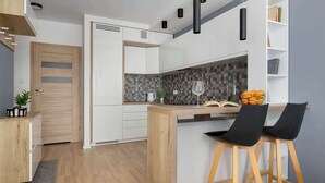 Eine moderne Küche mit weißen Schränken, einer Holzausziehtafel und einer Bar mit zwei schwarzen Barhocker.