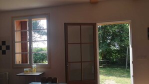A room with a large table, chairs, a window, and a door leading outside.