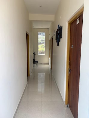 A corridor with a view of a garden through a window, a wooden door with a number, and a wall-mounted object. - Hotel Maitri (Dhanaulti)