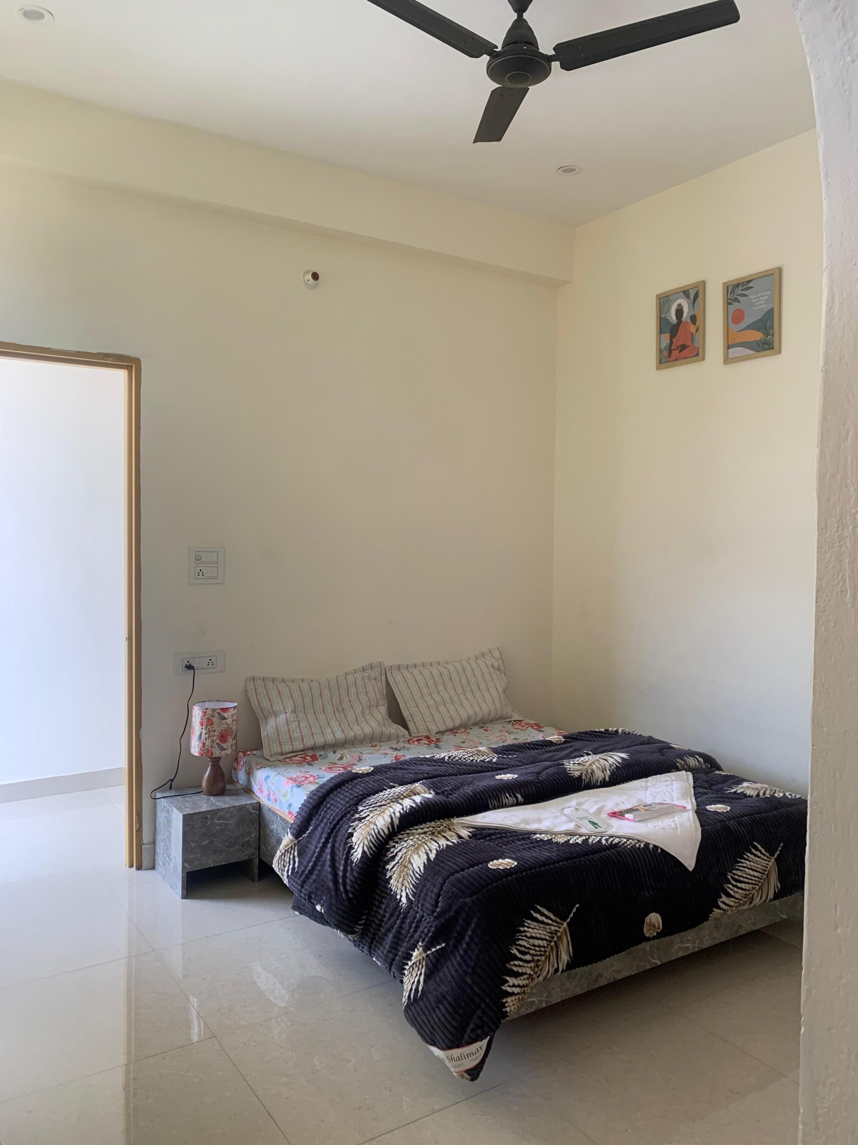 A bedroom with a bed, a ceiling fan, a nightstand, and two wall-mounted artworks.