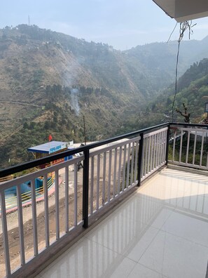 A balcony with a view of a hilly landscape, a small structure with a blue roof, and a flag. - Hotel Maitri (Dhanaulti)