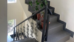 Un escalier avec des rampes et des marches noires, un pot de fleurs sur la droite et une fenêtre en haut.