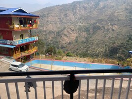 Un hotel con balcón, piscina y montañas al fondo.