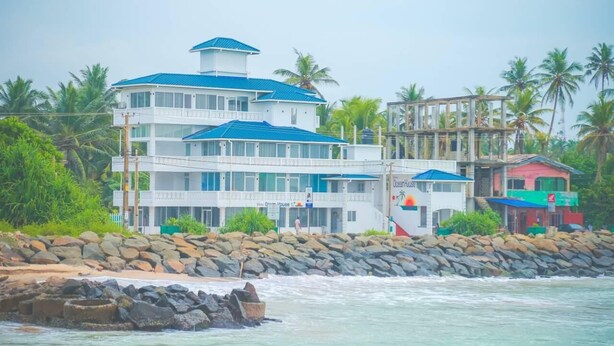 Una propiedad frente al mar de varios pisos, con un edificio blanco destacado y detalles azules, y una estructura roja cerca.
