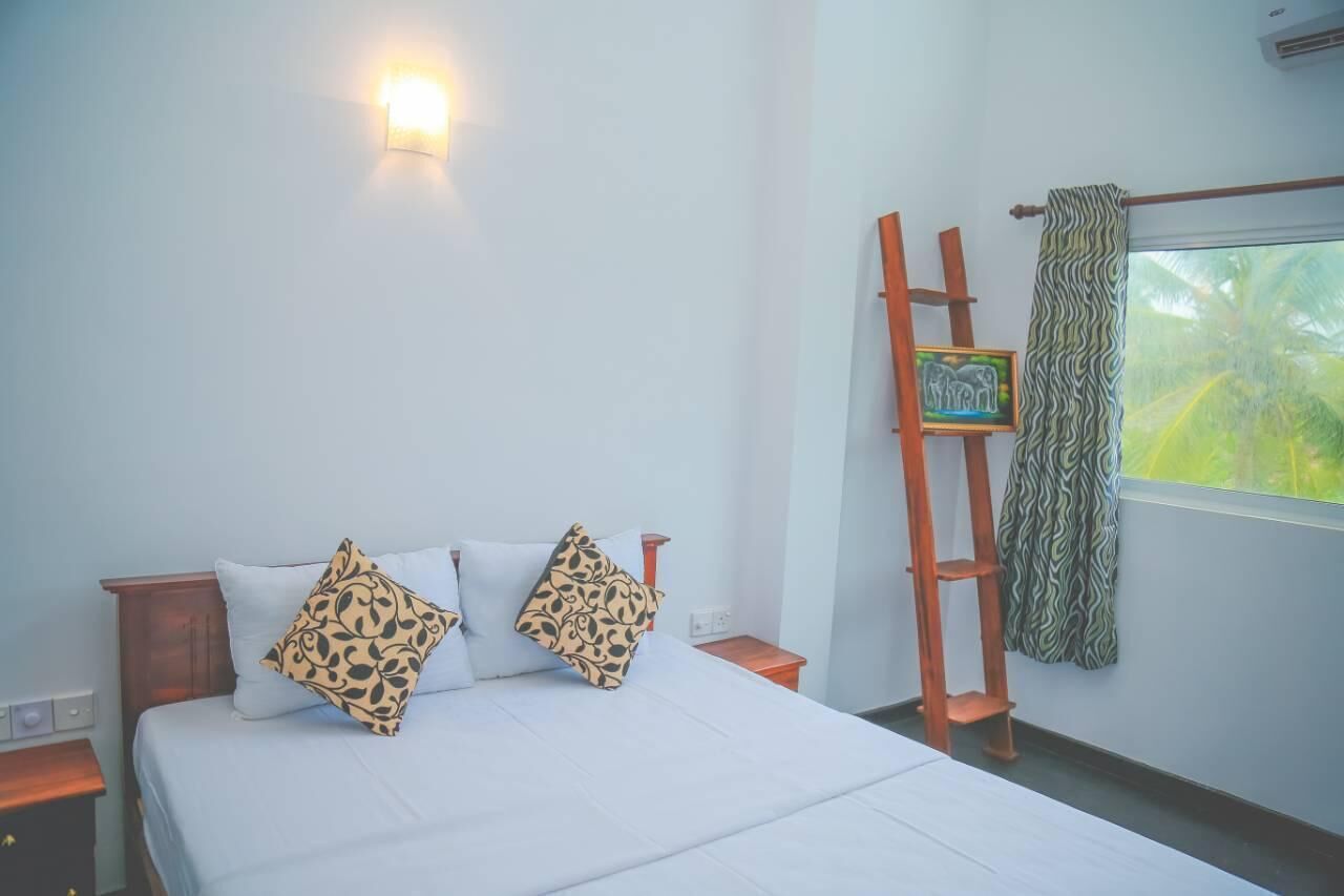 A bedroom with a bed, two pillows, a nightstand, a wall-mounted light, a ladder, and a window with a curtain.