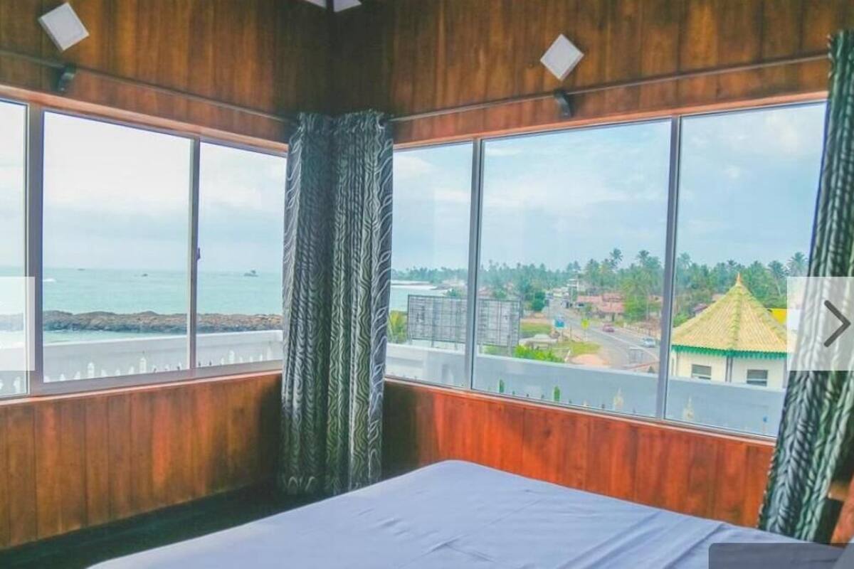 Quarto com uma janela grande que oferece vista para o mar e uma cidade ao longe.