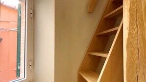 Een hoek van een kamer met een houten trap en een raam.