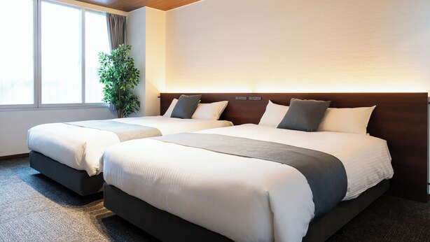 Ein Hotelzimmer mit zwei Betten, einem großen Fenster und einer Pflanze.