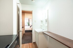 A narrow hallway leading to a bedroom with a bed, a bedside table, and a window. - Urban Stay LC12 Bankan (Sapporo)