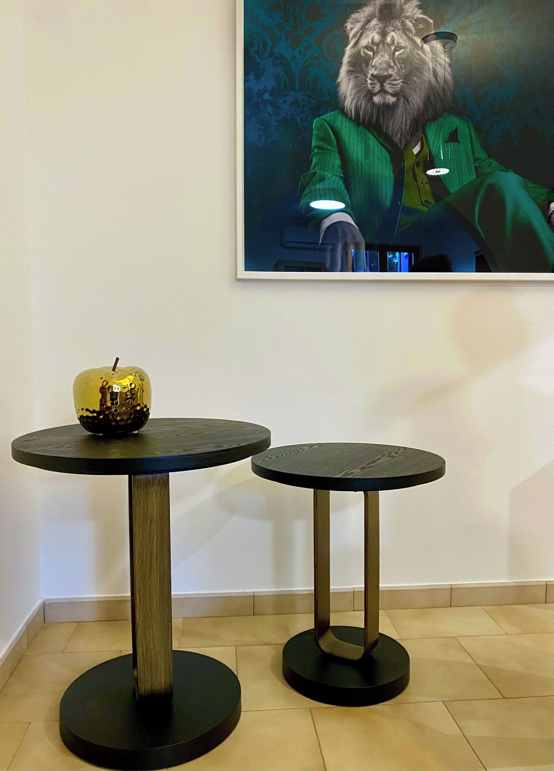 Two round tables with dark tops and metallic legs, placed on a tiled floor against a white wall.