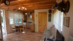 Un salon chaleureux avec un plancher en bois, un coin repas avec une table et des chaises, une cuisine avec des meubles en bois et une grande fenêtre avec des rideaux.