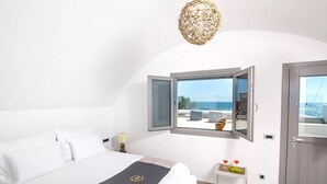 Un dormitorio con cama, ventana con vista despejada, una mesita con fruteros y una puerta.