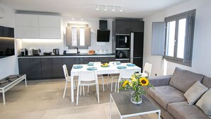 Una cocina moderna con armarios oscuros, una isla central y un comedor con sillas blancas y platos azules.