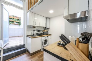 A compact kitchen with white cabinets, a washing machine, a microwave, and a wooden countertop. - Urban Loft with Character - Puerta de Toledo (Madrid)