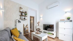 En moderne stue med en grå sofa, et hvidt sofabord, et fjernsyn og et hvidt skab.