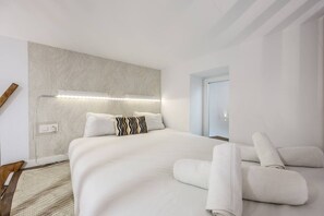 A modern hotel room with a large bed, a headboard with integrated lighting, a bedside table with a lamp, and a view of a cityscape through the window. - Urban Loft with Character - Puerta de Toledo (Madrid)