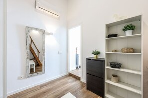 A hallway with a wooden staircase, a white-framed mirror, a black refrigerator, and a white shelving unit with plants and baskets. - Urban Loft with Character - Puerta de Toledo (Madrid)