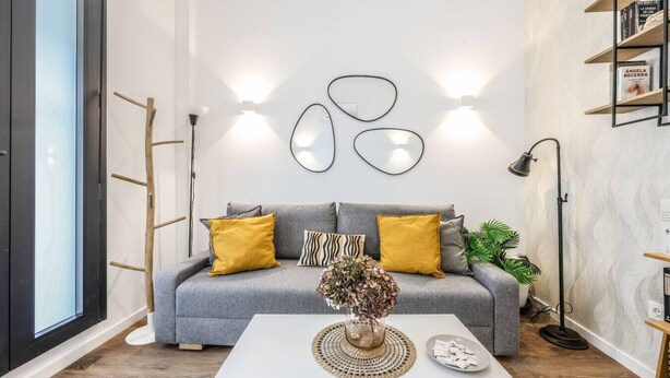 En moderne stue med en grå sofa, gule puder, et hvidt sofabord og en reol med bøger.