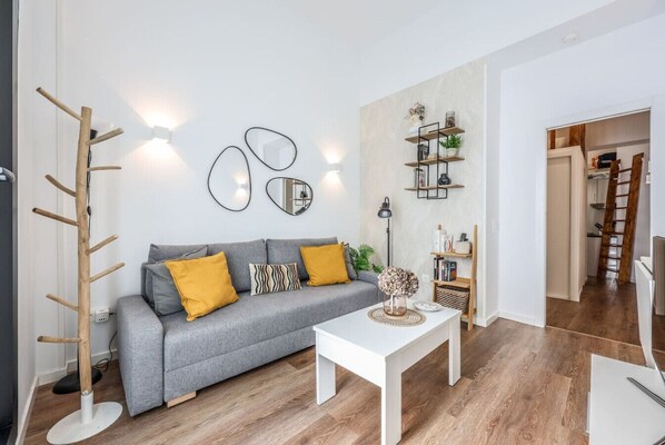 A modern living room with a grey sofa, yellow cushions, a white coffee table, and a wooden coat rack. - Urban Loft with Character - Puerta de Toledo (Madrid)