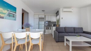 Una sala de estar moderna con un sofá gris, una mesa de centro blanca y una zona de comedor con sillas y una mesa blancos.
