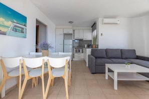 A modern living room with a gray sofa, a white coffee table, and a dining area with white chairs and a table. - Los Palmitos Peñiscola - 1 bedroom (Peñíscola)