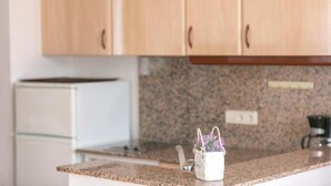 Una cocina con armarios de madera, encimera de granito y una pequeña olla blanca con flores moradas.