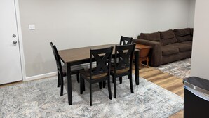 Uma sala de jantar com uma mesa e cadeiras de madeira, um sofá marrom e um tapete estampado.