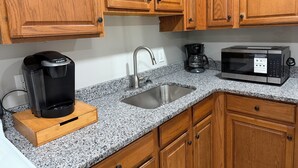Uma cozinha com armários de madeira, bancada de granito, cafeteira, jarra de café e micro-ondas.