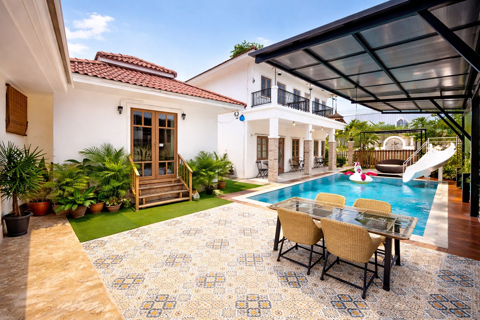 A poolside area with a covered patio, a dining table with chairs, and a staircase leading to a door.