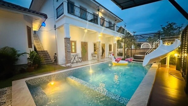 Une piscine avec un toboggan, un patio couvert et une maison à deux étages dotée d’un espace salon extérieur.