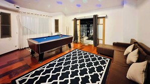 Une pièce avec une table de billard, un tapis à motifs, un canapé et un luminaire au plafond.