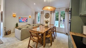 A spacious living area with a wooden dining table, comfortable seating, a large TV, and a decorative clock. - House between forest & beach on foot • Nordic bath (Jard-sur-Mer)